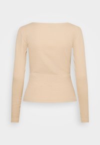 Beige långärmad topp i ribbad textur, med en figurnära silhuett och en bred fyrkantig halsringning, visad bakifrån mot en vit bakgrund.