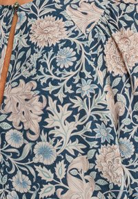 Tessuto a fiori nei toni del blu e crema, con intricati fiori e foglie, caratterizzato da un collo a chiave e una superficie texture.