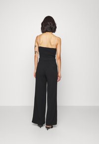 Svart jumpsuit med vida ben, som har en åtsittande överdel och tunna axelremmar. Tyget ser slätt ut, och det finns en subtil bälte-detalj vid midjan.