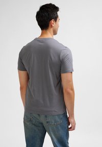 Grijze, kortekap t-shirt met een ronde hals en subtiele logo-detail op de schouder; gecombineerd met vervaagde blauwe jeans.