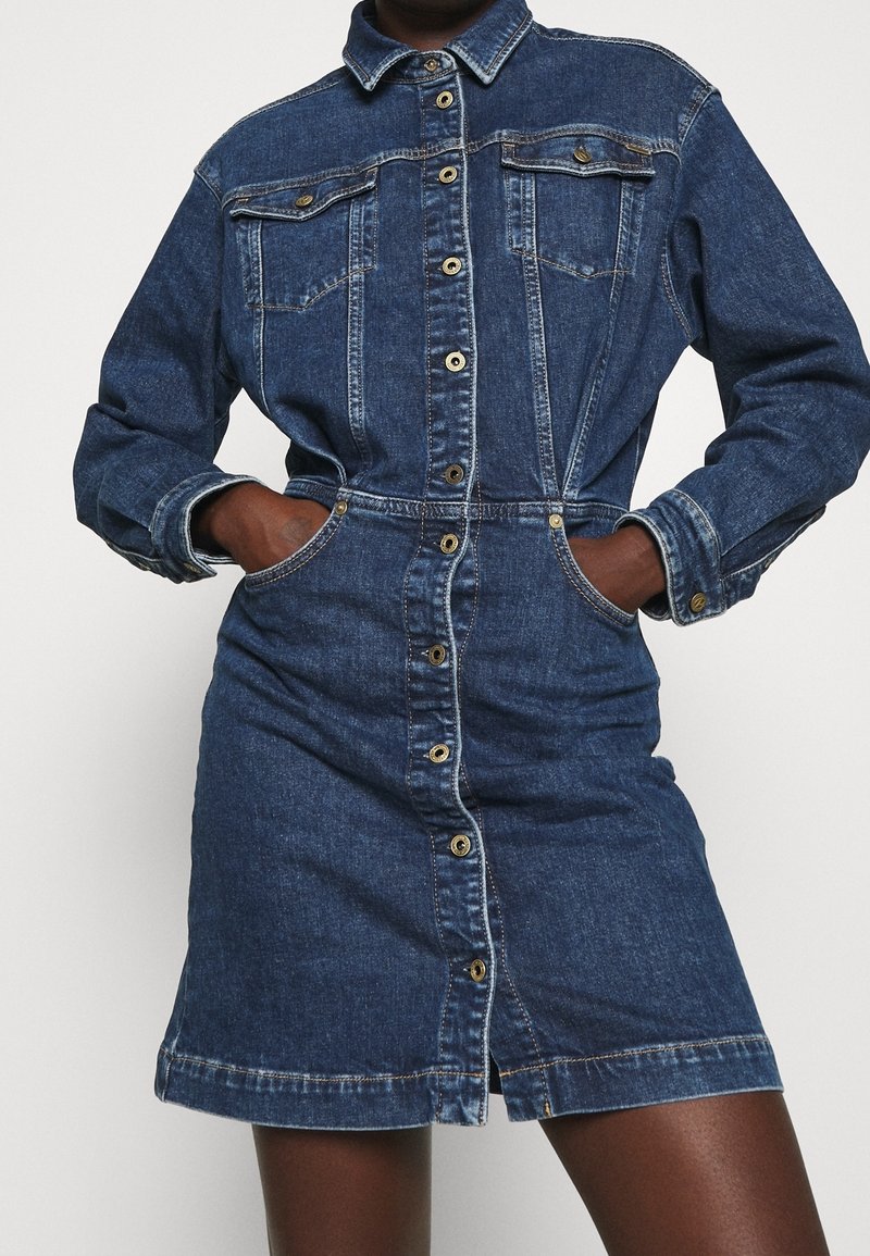 Jeanshemdkleid in Dunkelblau mit durchgehender Knopfleiste, Brusttaschen und seitlichen Taschen. Mit langen Ärmeln und einer taillierten Passform.