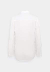 Chemise blanche à manches longues vue de dos avec un col droit et des poignets boutonnés sur un fond uni.