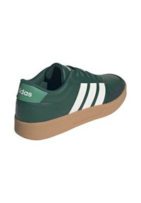 Sneakers sintetiche verdi con strisce bianche, caratterizzate da una finitura testurizzata, design con lacci, collarino imbottito e suola in gomma marrone.