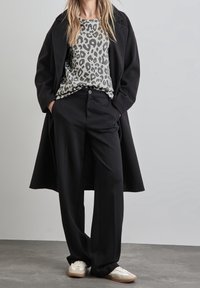 Manteau noir, chemise à imprimé léopard gris et pantalon noir ; tenue agrémentée de baskets blanches et d'une coupe décontractée ; texture de tissu lisse.