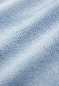 Tissu en denim bleu clair avec une surface lisse et légèrement texturée. Présente un motif de tissage classique et des variations subtiles de couleur.