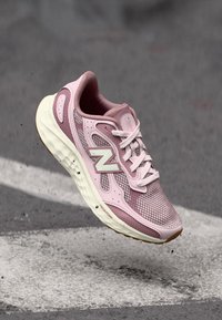 Light pink running shoe with mesh upper, padded collar, white accents, and a thick, cushioned sole. Features "N" logo on the side.