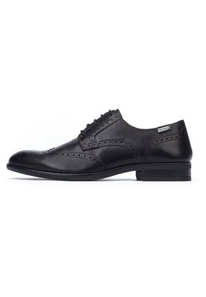 Zapato de vestir de cuero negro con detalles de brogue, puntera redonda y un tacón bajo y elegante. Los cordones se extienden desde la apertura del zapato.