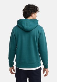 Sudadera con capucha en color verde azulado, hecha de una tela suave, que presenta un bolsillo tipo canguro y puños acanalados. La vista trasera muestra un corte relajado y detalles de costura.