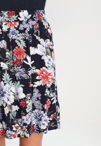 Floral skirt featuring a navy background with vibrant red, white, and blue flowers. Pleated design with an elastic waistband and smooth fabric texture.