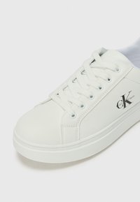 White leather sneakers featuring round toe, flat sole, and lace-up design. Notable accents include a small "CK" logo on the side.