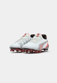 Soccer cleats with a white synthetic upper, red accents, textured design, and clear studs on a dark red sole. Black collar for ankle support.