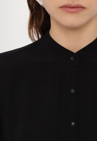 Cămașă neagră cu guler mandarin, cu embellishments subtile și nasturi negri rotunzi. Material neted cu un finisaj mat.