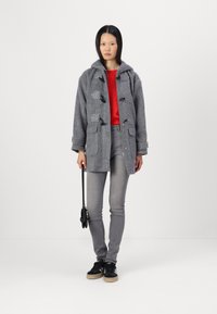 Abrigo duffle de lana gris con cierres de toggle, combinado con una camiseta roja, jeans grises y zapatillas negras. El abrigo tiene capucha y bolsillos.