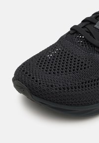 Chaussure de sport noire avec un dessus en maille tricotée respirante, présentant un motif en maille texturé et une semelle en caoutchouc lisse.