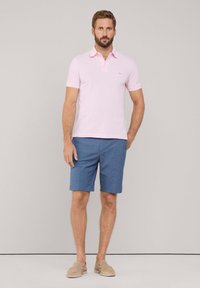Polo shirt rosa chiaro con colletto, abbinato a pantaloni corti blu. Calzature casual beige. Design semplice, senza motivi e con texture liscia.