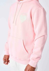 Felpa rosa realizzata in materiale morbido, con tasca frontale, cappuccio con coulisse e un dettaglio ricamato a forma di cuore sul petto.
