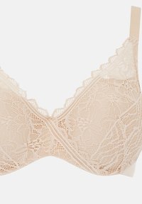 Koronkowy bralet w odcieniu nude z kwiatowymi wzorami, bezszwowy design, regulowane ramiączka oraz subtelne falbaniaste krawędzie. Charakteryzuje się miękką fakturą i gładkim wykończeniem.