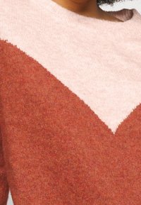 Sweter w kolorze rdzy z różowym wzorem w kształcie litery V na dekolcie, miękka tekstura i prążkowany kołnierz.