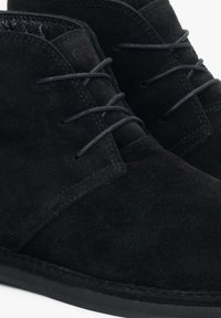 Czarne zamszowe botki za kostkę z okrągłym noskiem, sznurowadłami, teksturowaną cholewką i płaską gumową podeszwą. Widoczne przeszycia i subtelne oznaczenie marki.