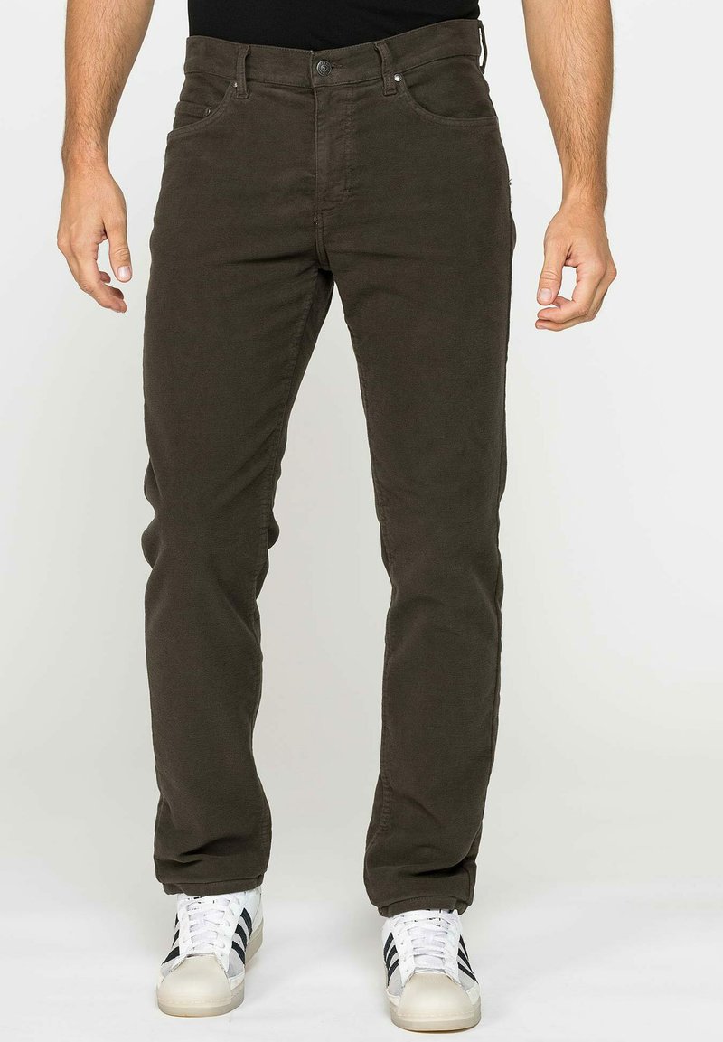 Pantaloni di cotone verde scuro con cinque tasche, design slim fit e un tessuto leggermente testurizzato. Abbinati a sneaker bianche con strisce nere.