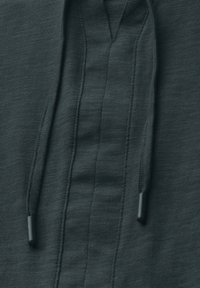 Dunkelgrauer Hoodie mit strukturiertem Stoff, einem V-Ausschnittdesign und Kordeln mit schwarzen Plastikspitzen. Saubere Nähdetails sind sichtbar.