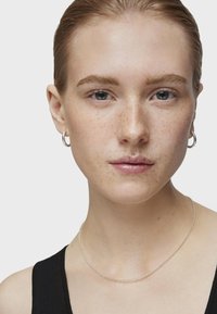 Collar de cadena de plata llevado con una blusa de canalé negra. Presenta un diseño delicado y un estilo minimalista, resaltando una elegante simplicidad.