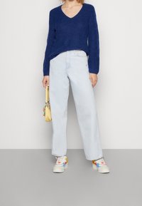 Granatowy sweter dzianinowy z dekoltem w serek, jasnoniebieskie spodnie z szerokimi nogawkami i wielokolorowe trampki. Uzupełnione małą żółtą torebką.