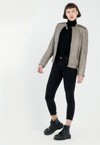Graue Lederjacke mit genietenen Schultern, Reißverschluss und taillierter Passform. Kombiniert mit schwarzen Jeans und schnürbaren klobigen Stiefeln.
