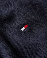 Mørk marineblå strikket stoff med et lite rektangulært brodert logo i rød, hvit og svart tråd.