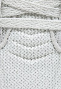 Baskets blanches avec une tige en maille texturée, dotées de lacets épais et tressés ainsi qu'une section de bout lisse et arrondie.