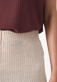 Burgundy ribbad topp lager på en krämfärgad ribbad kjol, båda med vertikala ränder och en texturerad yta. Närbild av tyg och sömmar.