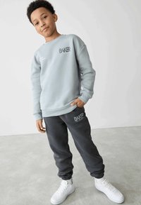 Lys grå sweatshirt med "BAKER" logo, parret med mørkegrå joggers med matchende logo og hvide sneakers. Blødt, afslappet stof.