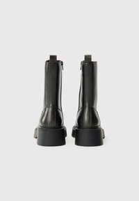 Black leather ankle boots with a rounded toe, vertical stitching details, and a thick, textured rubber sole. Includes zip fasteners.