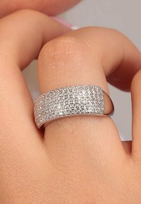 Anello in argento con più file di piccoli cristalli trasparenti, caratterizzato da una superficie liscia e lucida e una forma arrotondata.