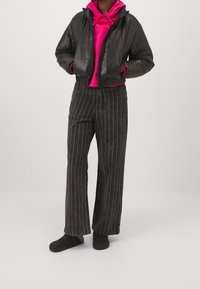 Svart vadderad jacka, kort design, kombinerad med en rosa hoodie och vida svarta byxor med ränder. Svarta träskor kompletterar outfiten.