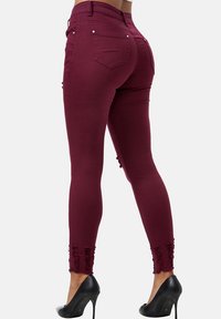 Jeans skinny burdeos con una cintura alta, con dobladillos desgastados y bolsillos traseros, hechos de un material de mezclilla elástico.