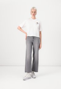 Hvit avkortet t-skjorte med grafisk trykk, i kombinasjon med høyt liv, vide grå jeans og hvite sneakers. Enkelt design, uformell stil.