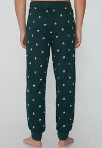 Donkergroene sweatpants van zachte stof, met een patroon van cirkelvormige ontwerpen in het wit en zwart. Elastische tailleband en boorden.