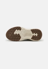 Semelle de chaussure avec une semelle en caoutchouc brun et blanc texturée présentant des motifs en losange et le mot « Vibram » embossé au centre.