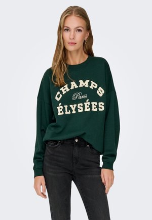 Sweat à capuche vert avec du texte embossé blanc : "CHAMPS ÉLYSÉES Paris." Il a des manches longues et une coupe décontractée, associé à un jean noir.