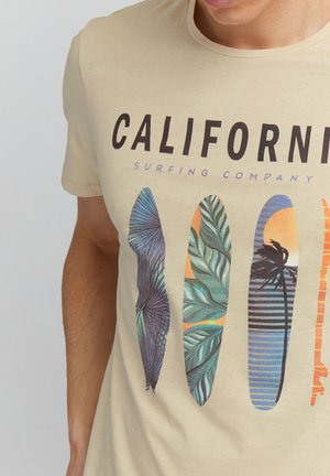 Beiges T-Shirt mit dem Schriftzug "CALIFORNIA SURFING COMPANY" und vier bunten Surfbrett-Designs mit Palmenblättern und Sonnenuntergangsmustern.