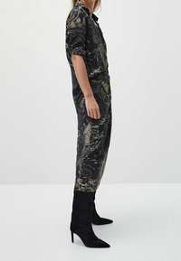 Black patterned jumpsuit with short rolled sleeves, cinched waist, and tapered legs, paired with black suede over-the-knee boots.