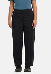 Schwarze, leichte, elastische Hosen mit lockerer Passform. Glatte Textur mit klassischem Design, kombiniert mit grauen Sportschuhen.