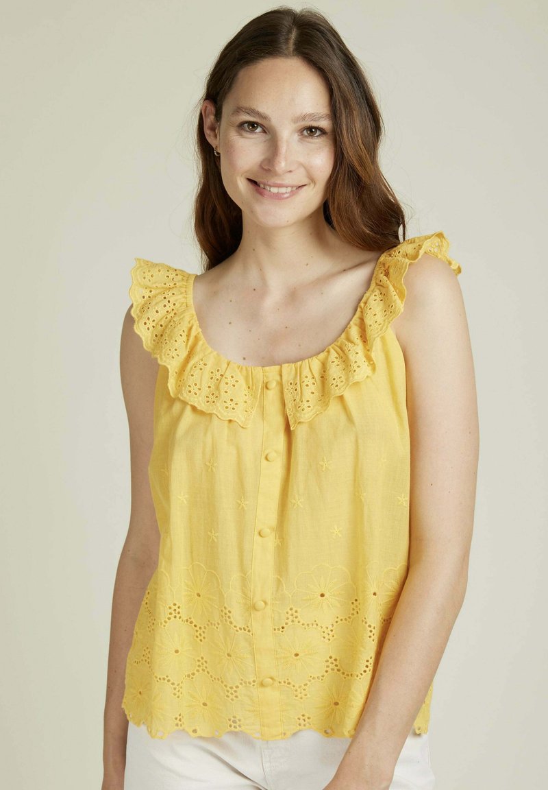 Blouse sans manches jaune avec un col à volants,broderies florales et bouton sur le devant. Tissu léger avec un ourlet festonné et des détails.