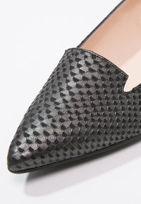 Chaussure plate noire pointue avec un motif texturé en forme d'écailles et une petite encoche en forme de V sur le bord supérieur.