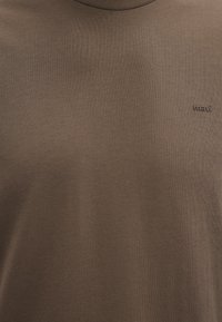 Braunes Rundhals-T-Shirt aus weichem Baumwollmix. Verfügt über eine dezente Rippstruktur und ein kleines, tonal gehaltenes Logo auf der Brust.