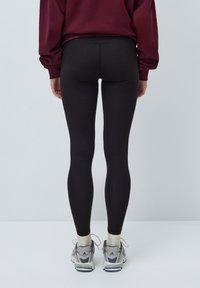 Svarte tights laget av elastisk stoff, med høy midje og en glatt tekstur, kombinert med grå og hvite sportssko.