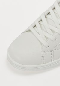 Hvite lærersneakers med flate hvite snørebånd, rund tå og subtile sømdetaljer. Glatt tekstur og formet gummisåle.