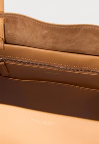 Εσωτερικό από τσάντα χειρός με δέρμα ταμπά, με λεία υφή, τσέπη με φερμουάρ και επένδυση από σουέντ με ραφές λεπτομέρειες. Το λογότυπο είναι ορατό.