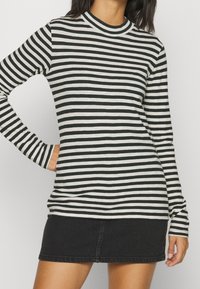 Schwarz-weiß gestreiftes langärmeliges Oberteil mit hohem Kragen, kombinierte mit einem schwarzen Jeansrock. Der Stoff wirkt weich und körpernah.